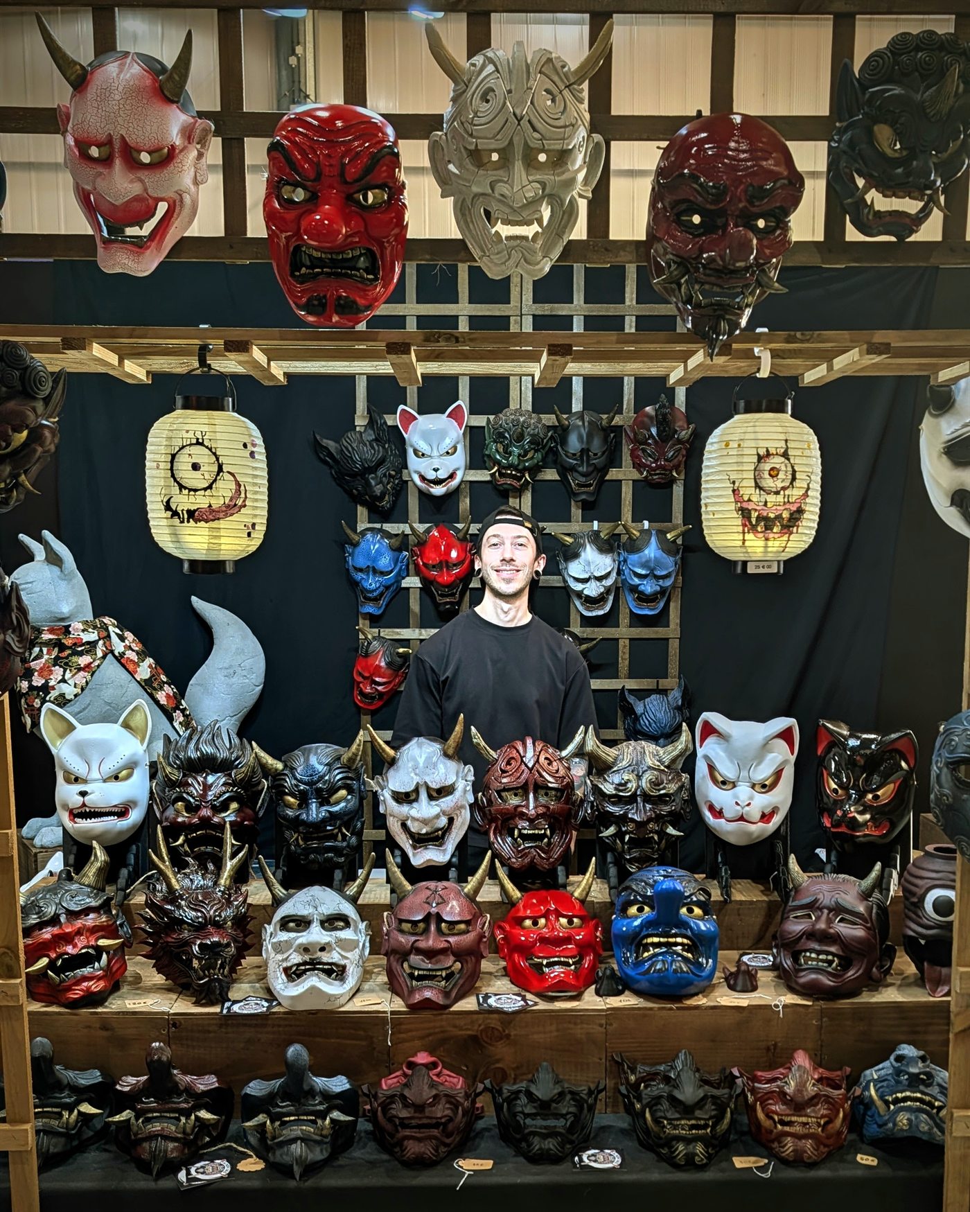 Jérémy sur le stand Dai Yokai entouré de masques Oni, Kitsune, Tengu et Hannya