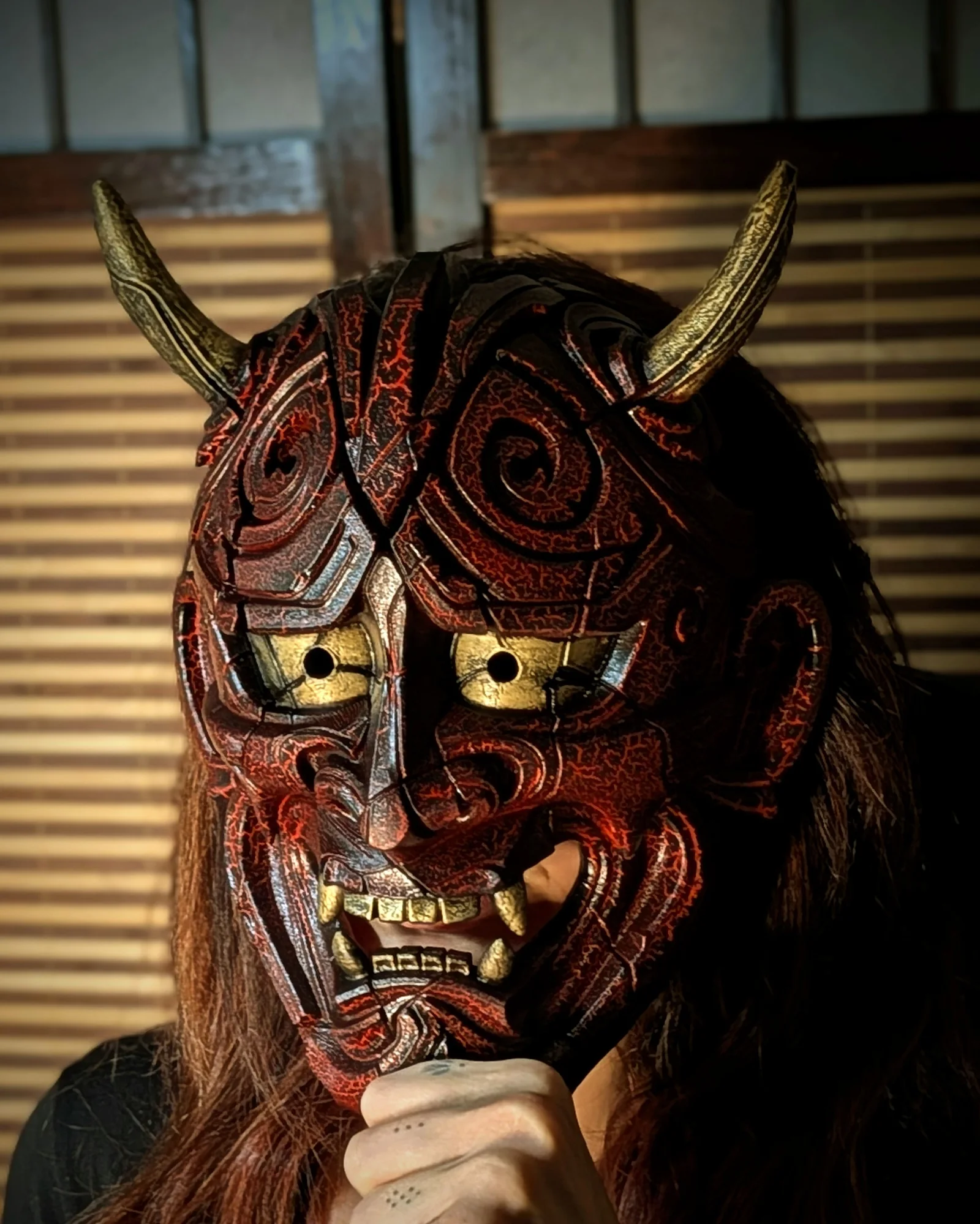 Red and black Dai Yokai Kezurata Hannya mask worn in close-up, cracked reliefs visible.
