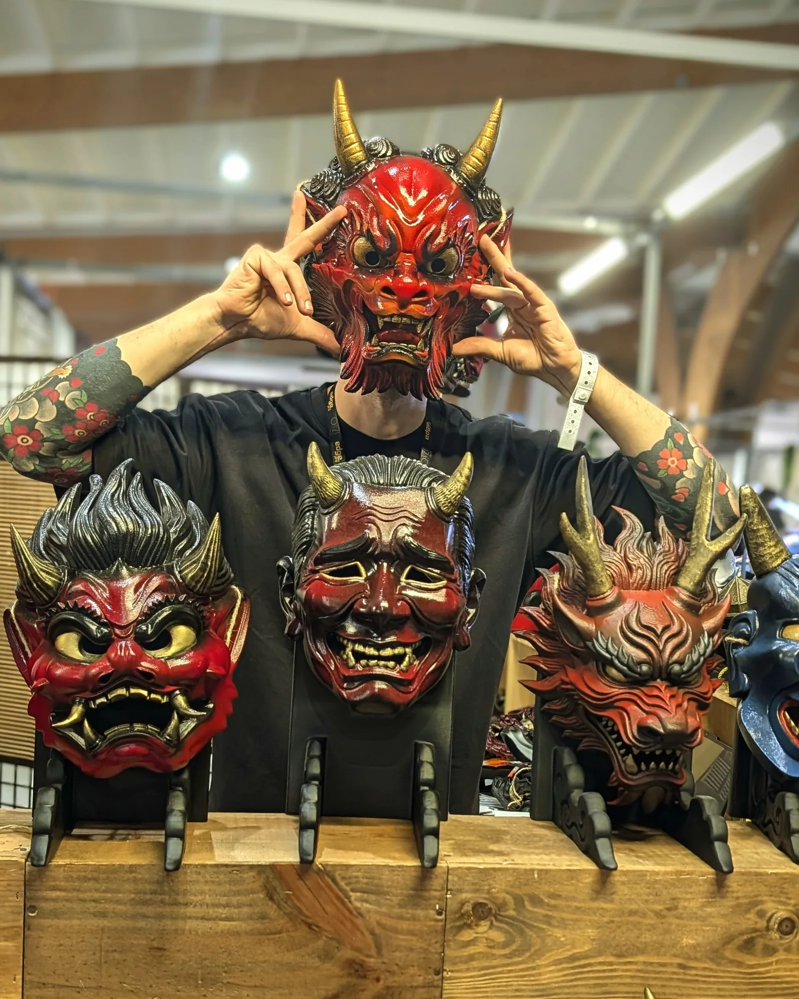 Red Dai Yokai Oni mask worn, surrounded by Japanese masks displayed on stands.