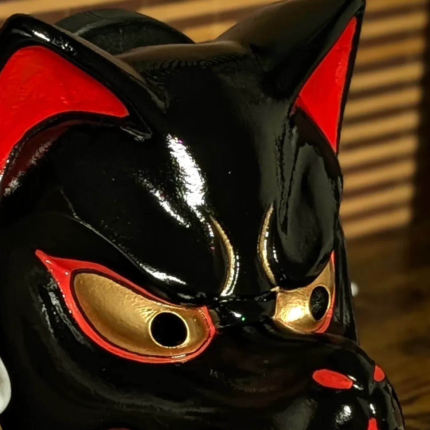 Gros plan sur le visage du masque Kitsune noir traditionnel, yeux dorés et peinture brillante.