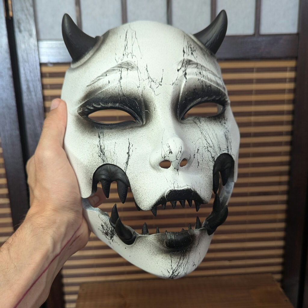 Masque Kuchisake Onna avec mâchoire ouverte révélant le sourire fendu sanglant et les dents pourries.