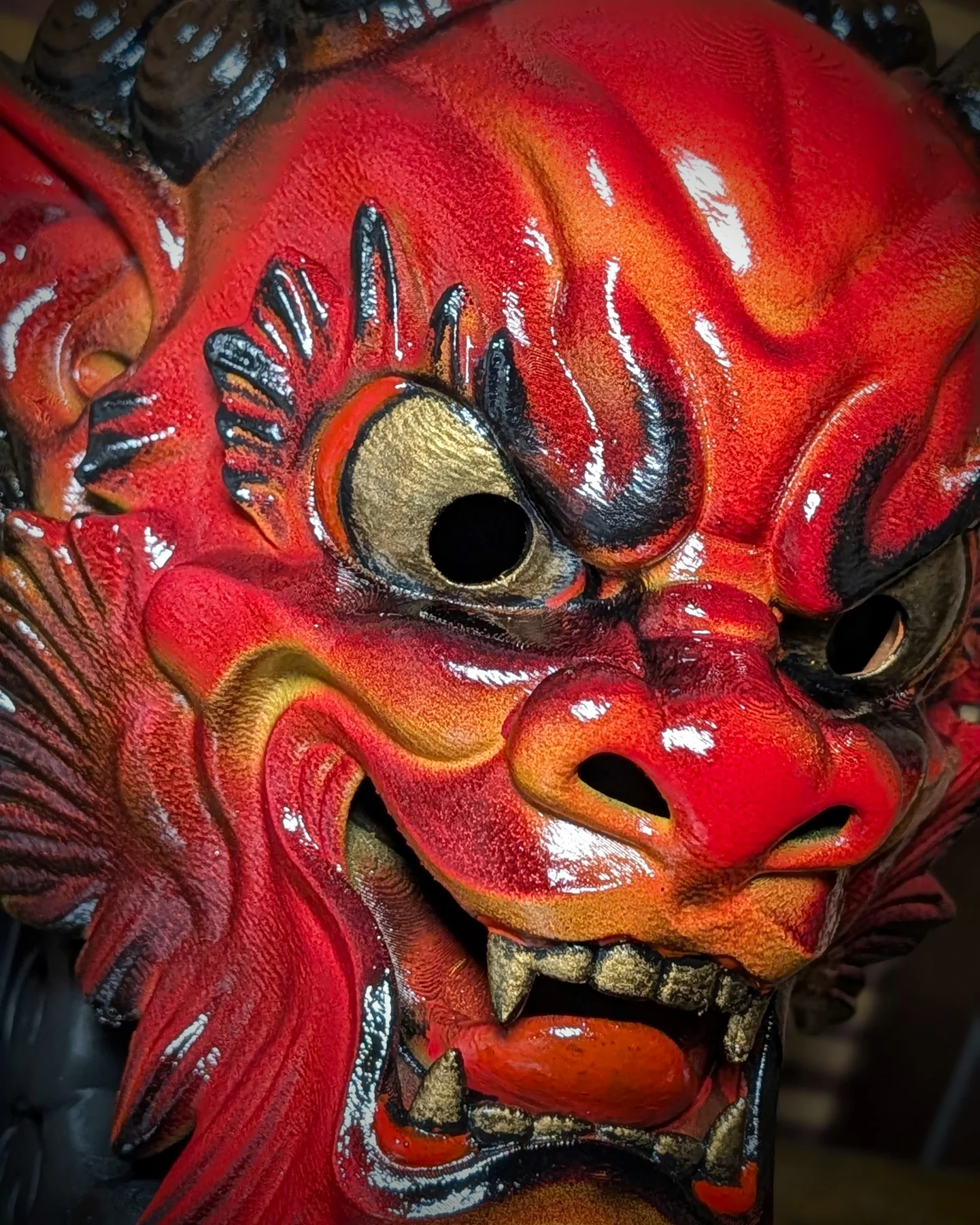 Close detail of the face of a handmade red Irezumi Oni Mask, with glossy paint and gold details.