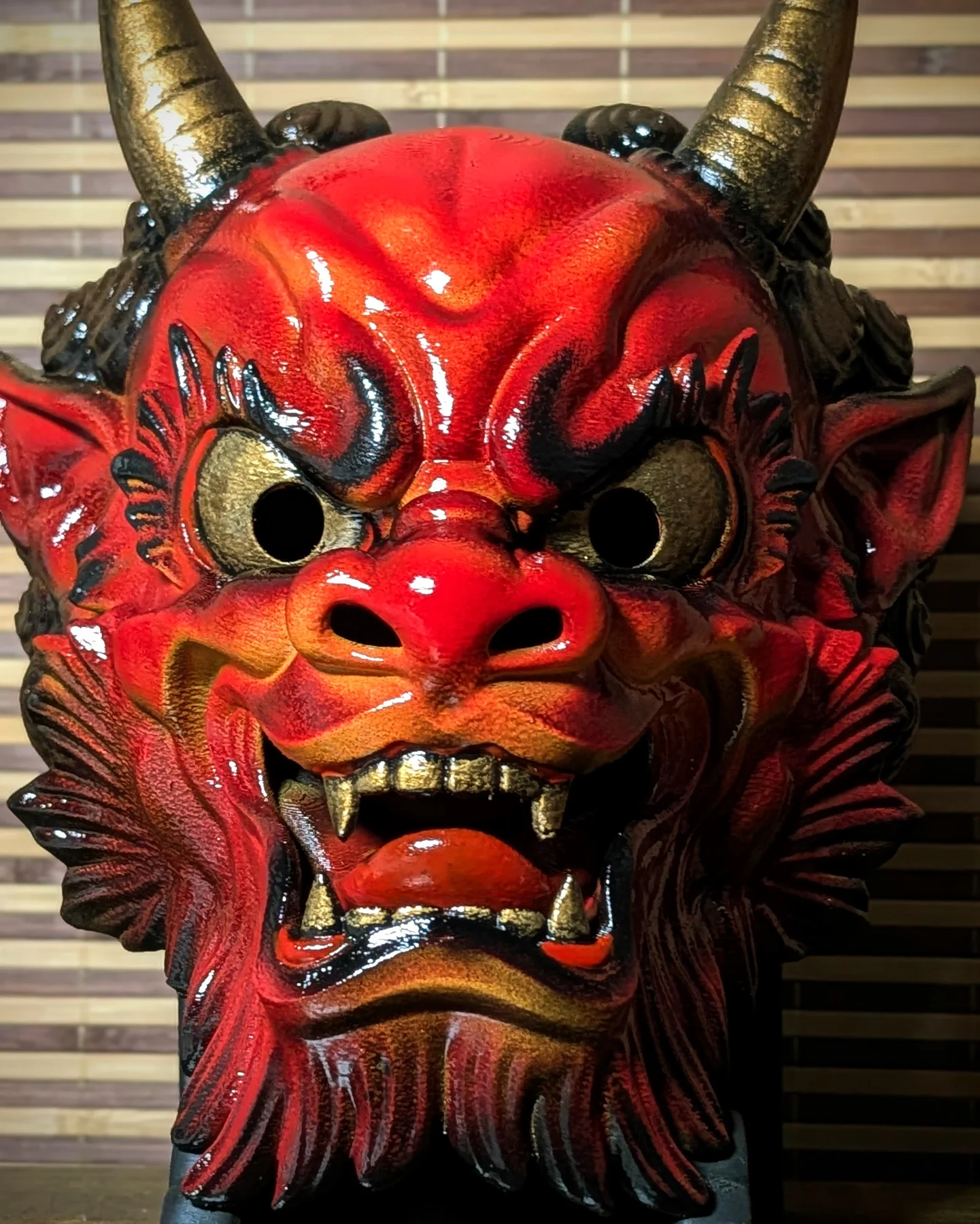 Front close-up of a handmade Irezumi Oni Mask with gold horns, black shadows and red glossy paint.